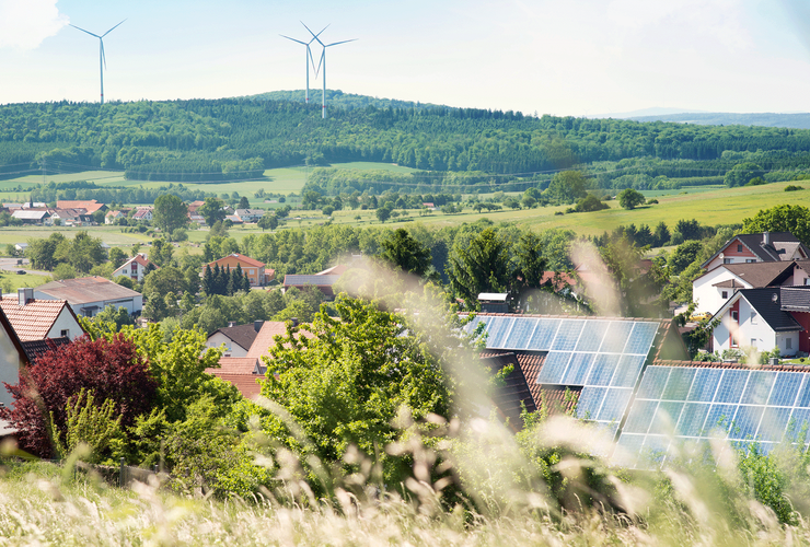 Landschaft mit Häusern mit PV-Anlage und Windrädern im Hintergrund